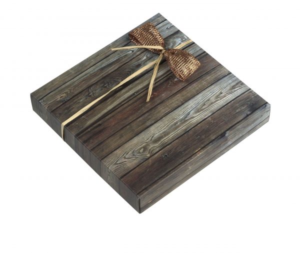 16er Schachtel "Triologie Nougat" von Schell Schokoladen. Die Verpackung hat ein hellgraues Holzmuster mit einer braunen kleinen Schleife gebunden.