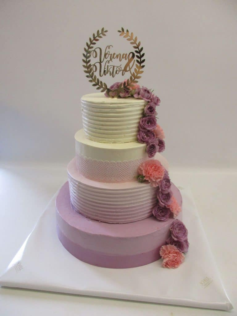 Vierstöckige Cremetorte in lila, pink und gelb mit rosa Tortenspitze, Rüschchen, Schriftzugstecker und lila Rosendekor von Schell Schokoladenr