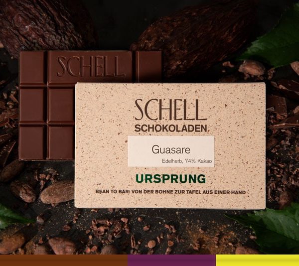 Es ist die Guasare Schokolade zu sehen über der Schokolade ist die beige Verpackung wo der Name und unser Logo abgebildet ist.