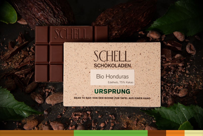 Es ist die Bio Honduras Schokolade zu sehen über der Schokolade ist die beige Verpackung wo der Name und unser Logo abgebildet ist.