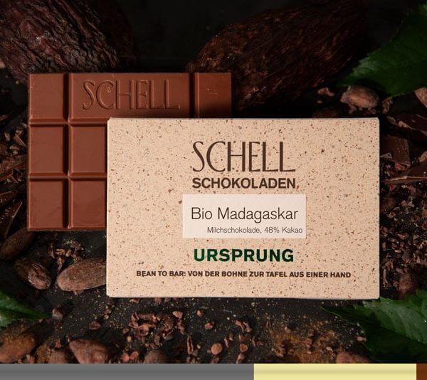 Es ist die Bio Madagaskar Schokolade zu sehen über der Schokolade ist die beige Verpackung wo der Name und unser Logo abgebildet ist.