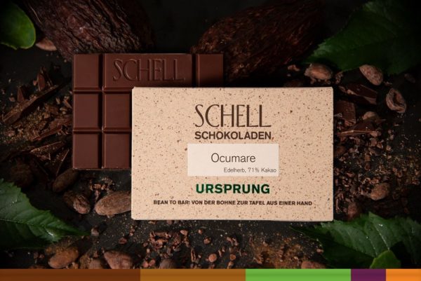 Es ist die Ocumare Schokolade zu sehen über der Schokolade ist die beige Verpackung wo der Name und unser Logo abgebildet ist.