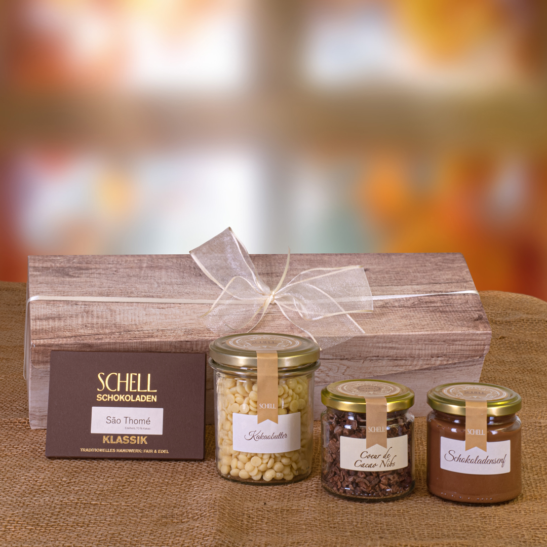 Geschenkpaket Schokokochbox enthält eine Tafel Sao Thome in einer braunen Verpackung, Kakaobutter, Coeur de Cacao Nibs und Schokoladensenf im Glas.