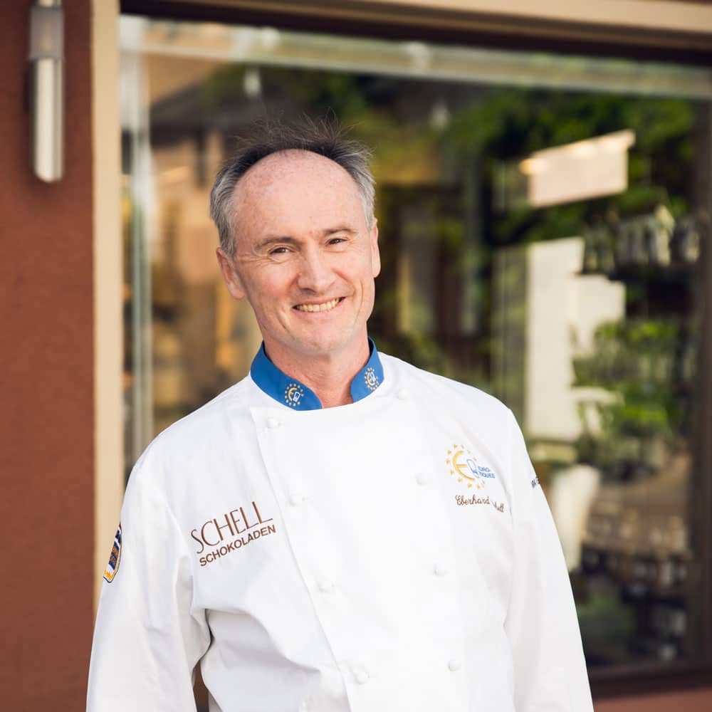 Es ist der Chef von SCHELL Schokoladen abgebildet der Eberhard Schell wie er vor dem Café steht.
