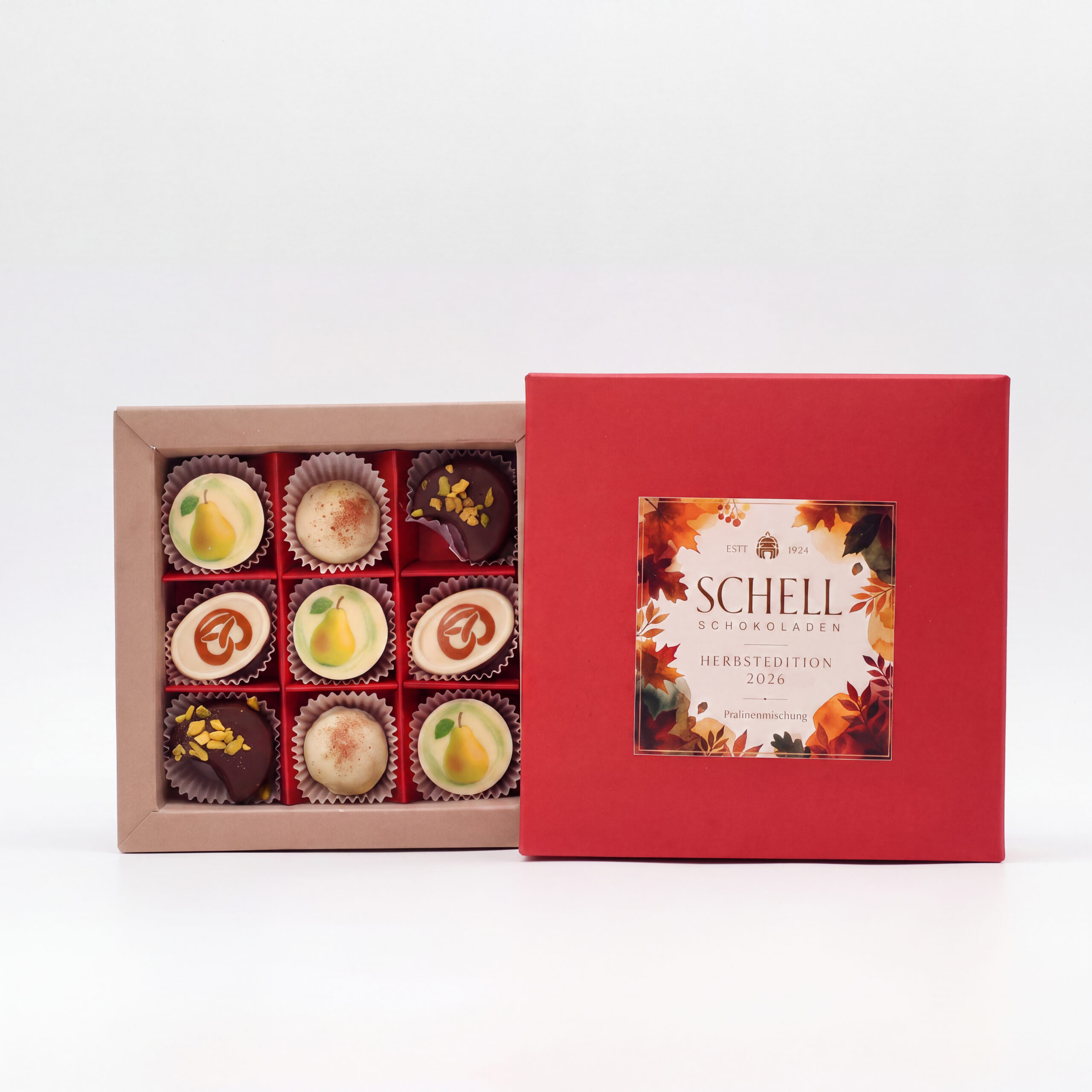 Geöffnete 9er-Pralinenbox von Schell Schokoladen mit neun Pralinen in drei Reihen neben rotem Deckel mit Herbstmotiv.
